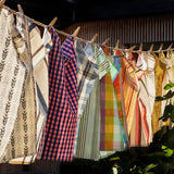Collection of patterned tea towels hanging on a clothesline outdoors.