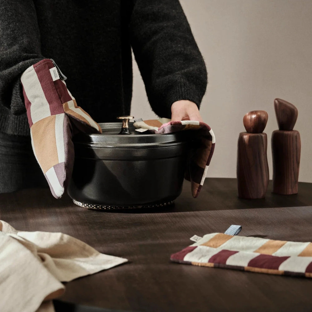 Person lifting a dark pot with a patchwork oven glove in a kitchen