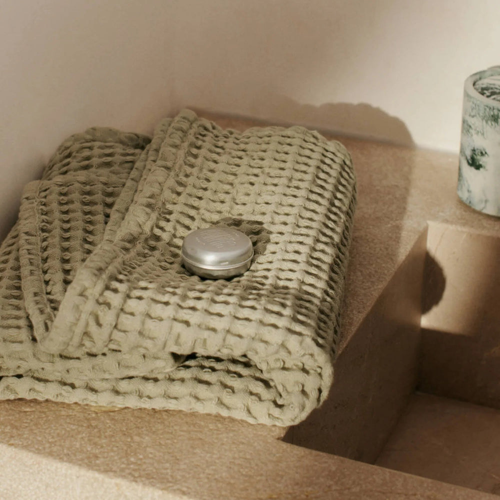 Organic Hand Towel, Light Celedon by ferm LIVING, folded beside a bath