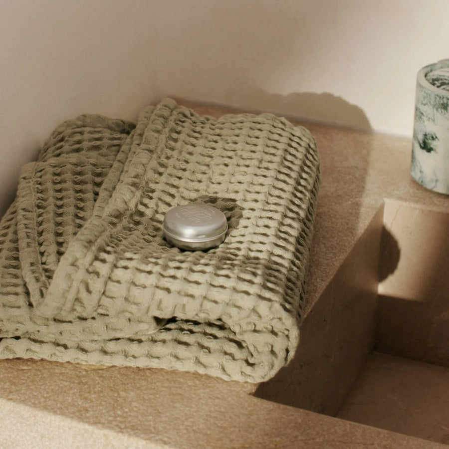 Organic Hand Towel, Light Celedon by ferm LIVING, folded beside a bath