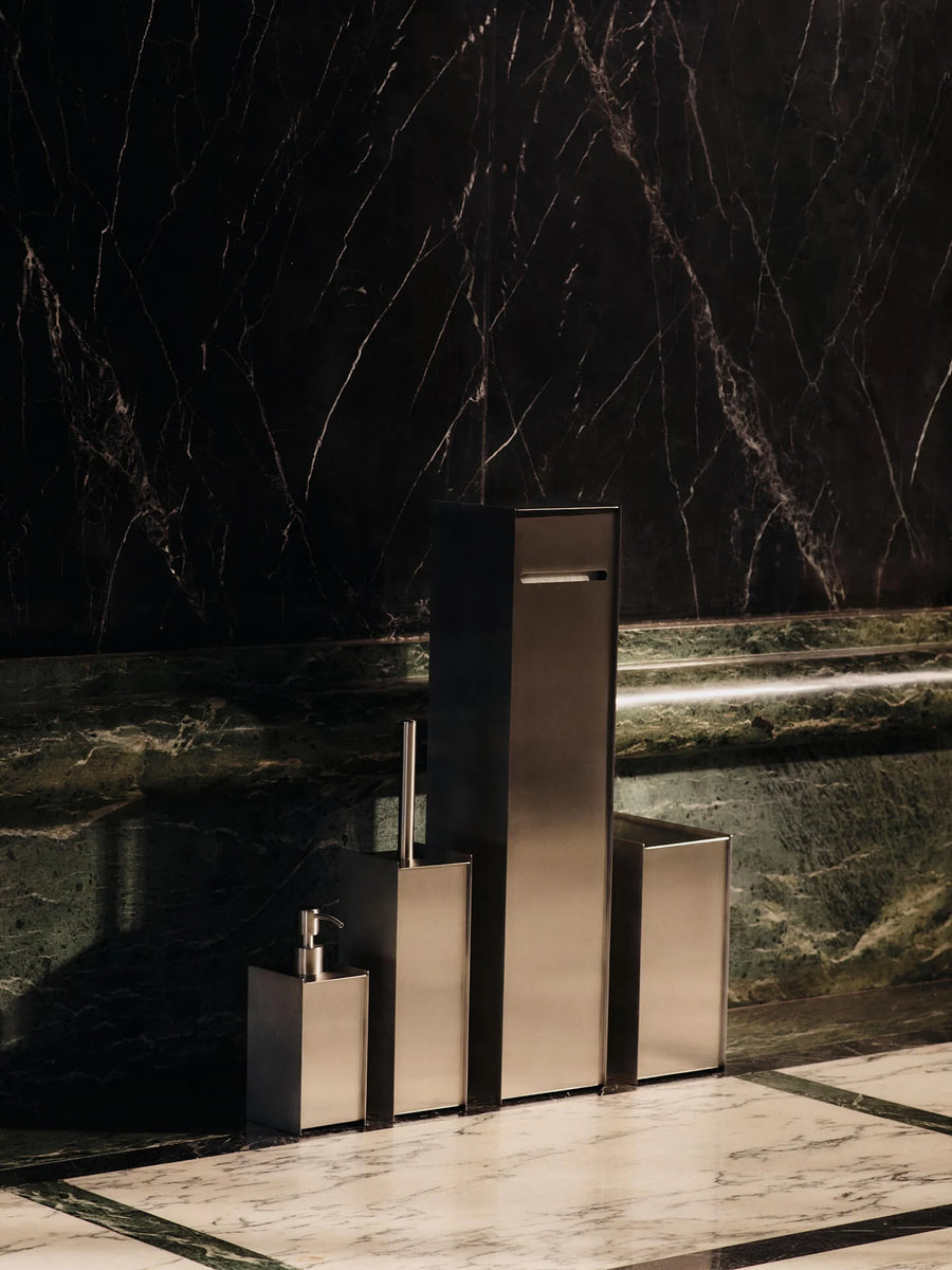 Sama Toilet Paper Dispenser, Brushed Stainless Steel by ferm LIVING, in a dark bathroom