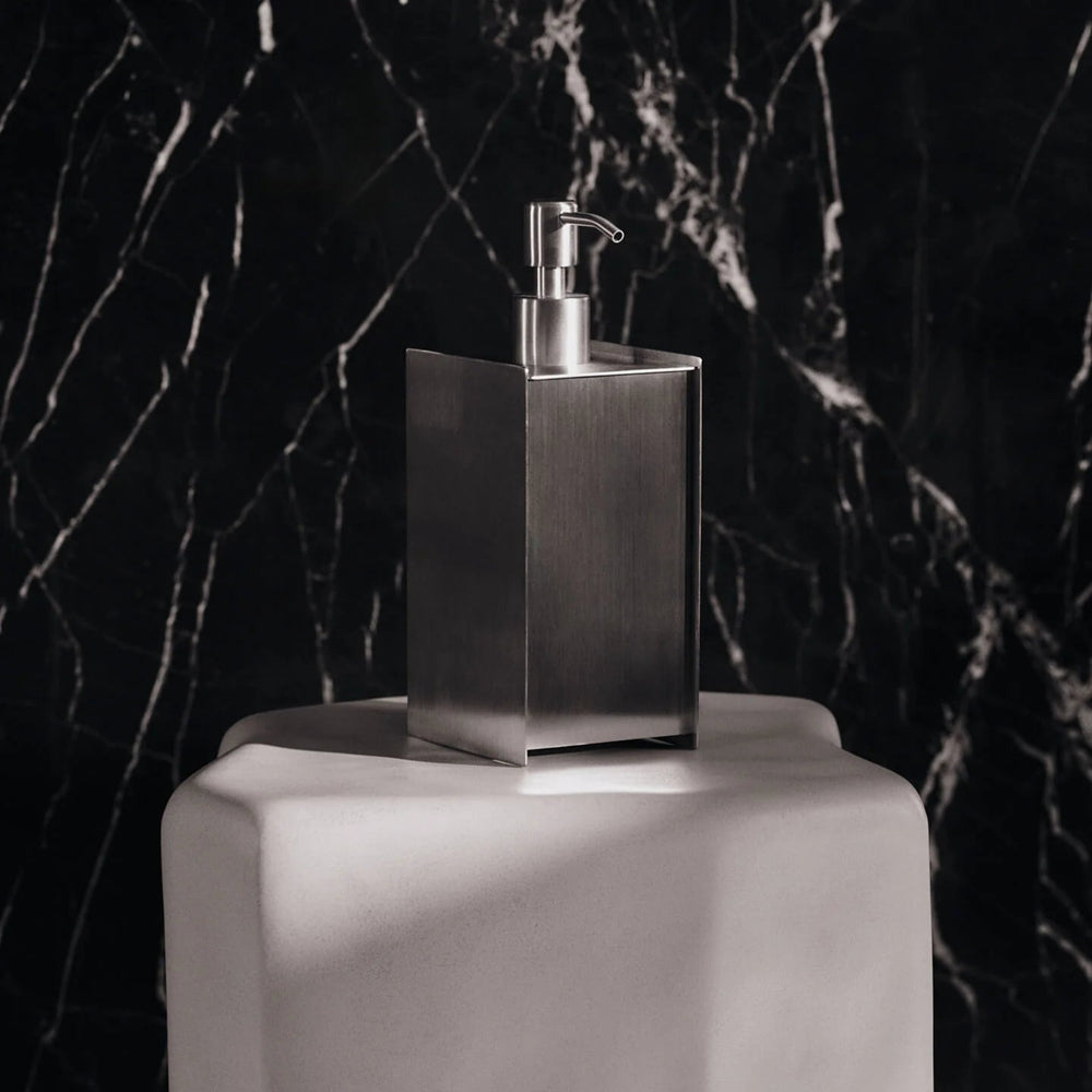 Sama Soap Dispenser, Brushed Stainless Steel by ferm LIVING, against dark marble