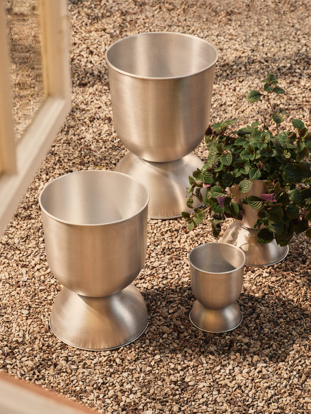 Hourglass Pots, Various Sizes, Aluminium by ferm LIVING, on gravel with a plant