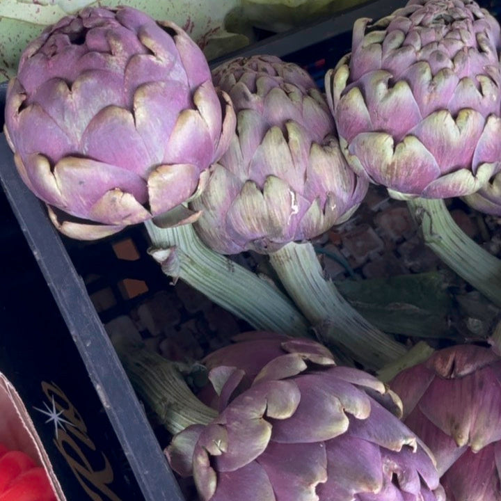 Carciofo Scented Candle, 250ml by Earl of East, lit among purple artichokes