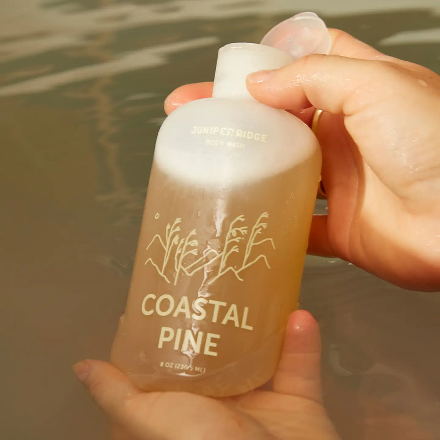 Hand holding a Coastal Pine body wash bottle