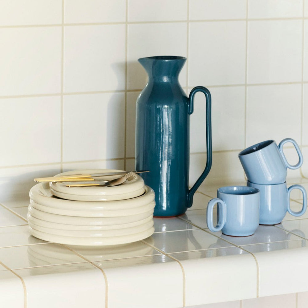 Barro Plate Set of Two, Ø18, Off-White by HAY, stacked beside a jug and cups on tiles