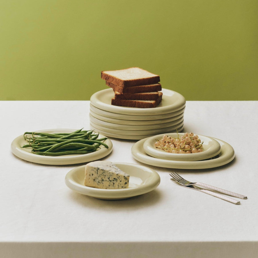 Barro Plate Set of Two, Ø24, Pistachio by HAY, stacked with bread and beans on an olive backdrop