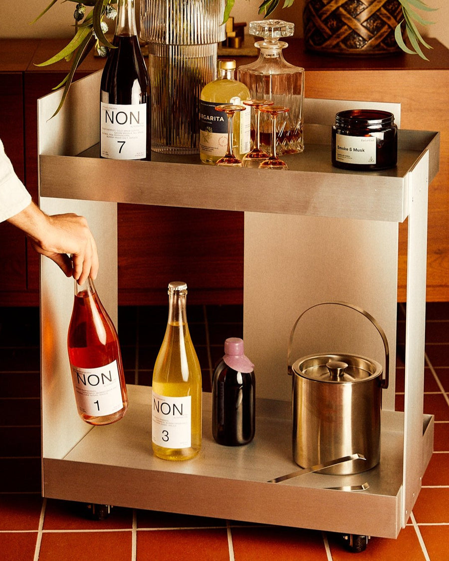 Lager Trolley, Aluminium by ferm LIVING, holding drinks against an orange wall