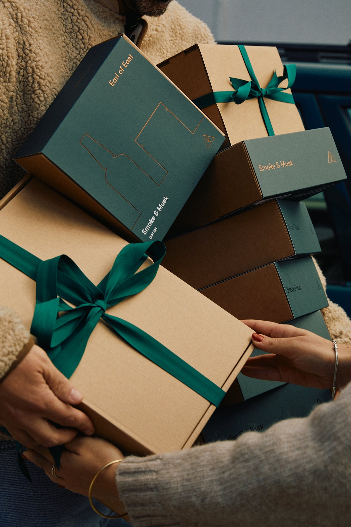 Person carrying a stack of Earl of East gift boxes tied with green ribbon