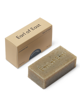 A beige-colored cleansing soap bar with 'Earl of East' engraved on it, accompanied by its packaging