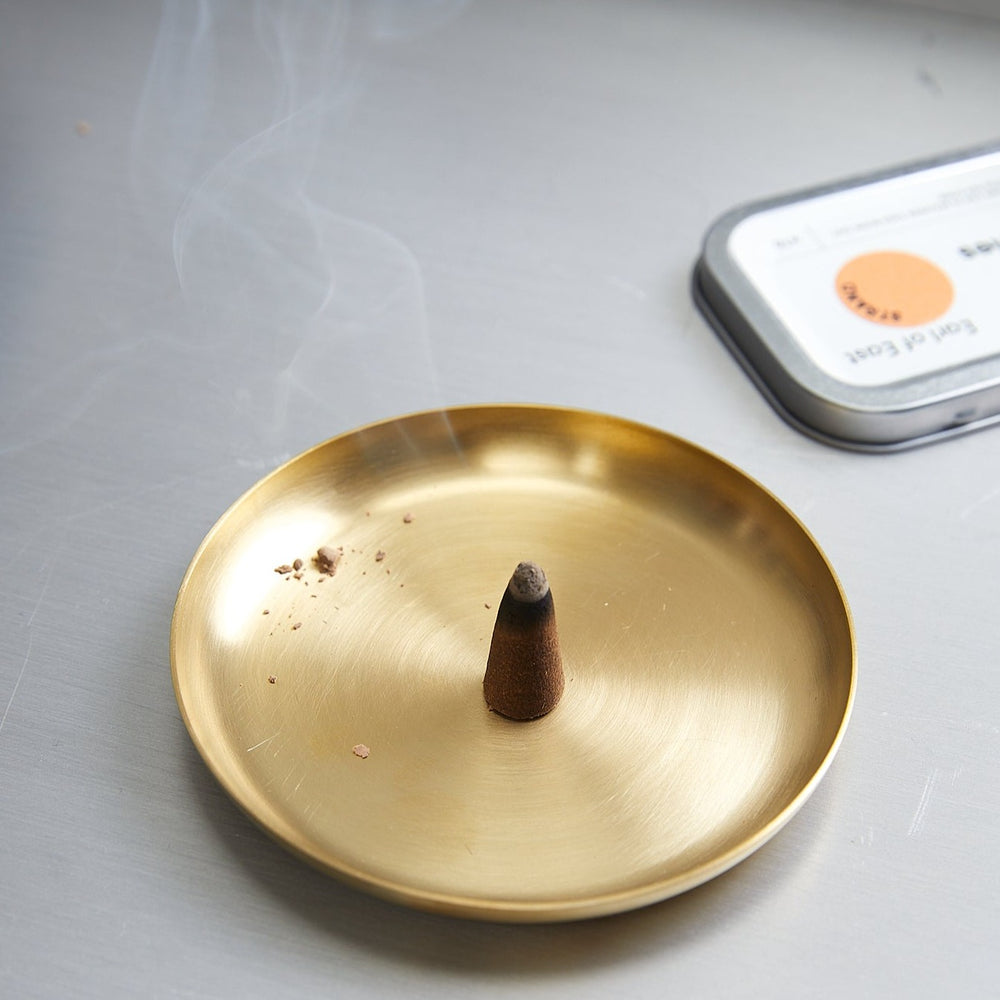 Basho Tray Round, Brass by ferm LIVING, holding a burning incense cone