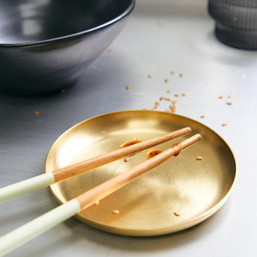 Basho Tray Round, Brass by ferm LIVING, holding chopsticks on a grey table