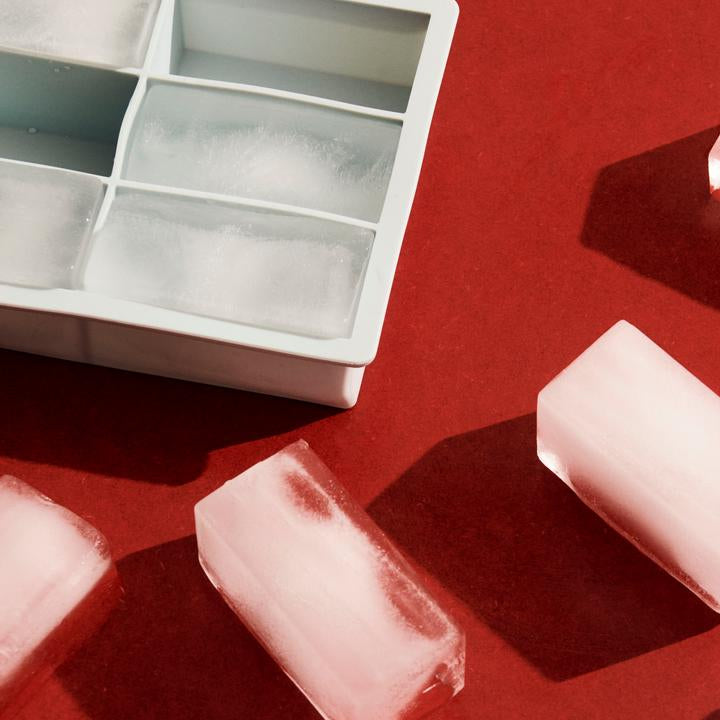 Ice cubes on a red surface with two ice cube trays.
