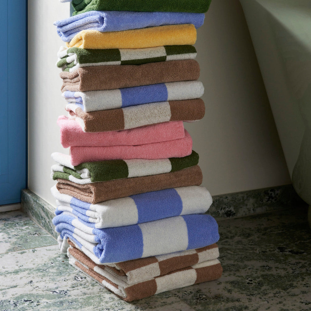 Mono Bath Towel, Cappuccino by HAY, stacked in a range of colours in a bathroom