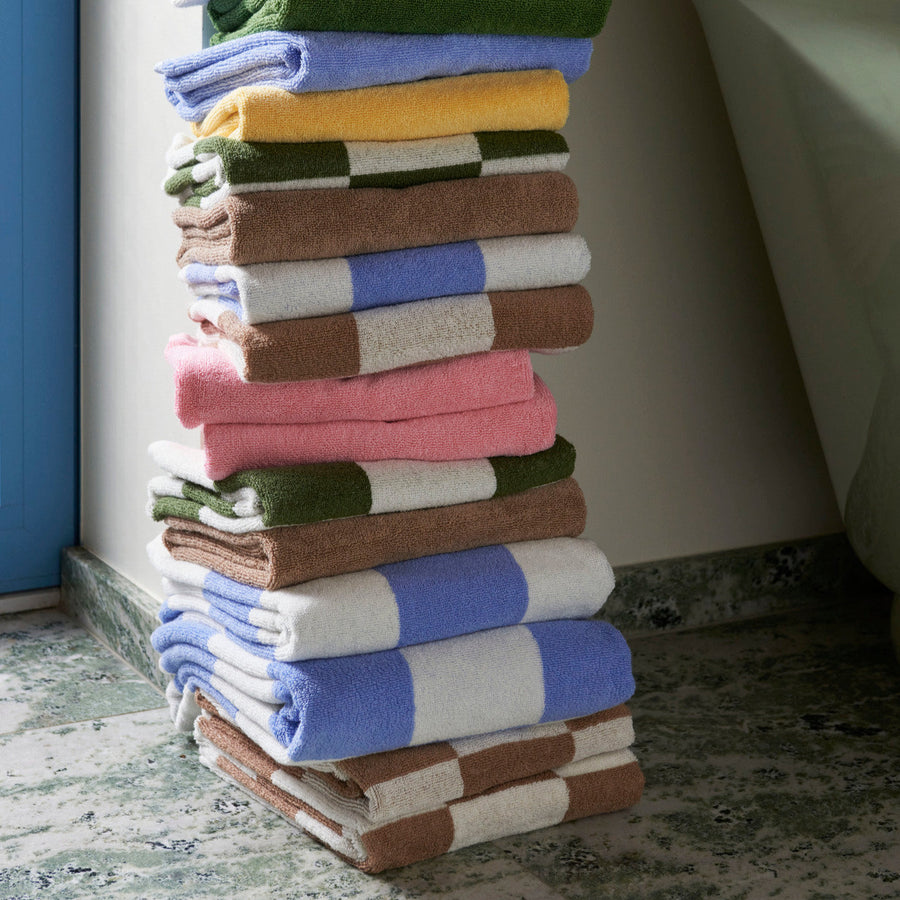 Mono Bath Towel, Cappuccino by HAY, stacked in a range of colours in a bathroom