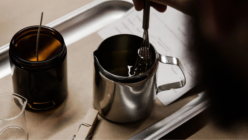 Candle wax being poured from a steel jug into a jar