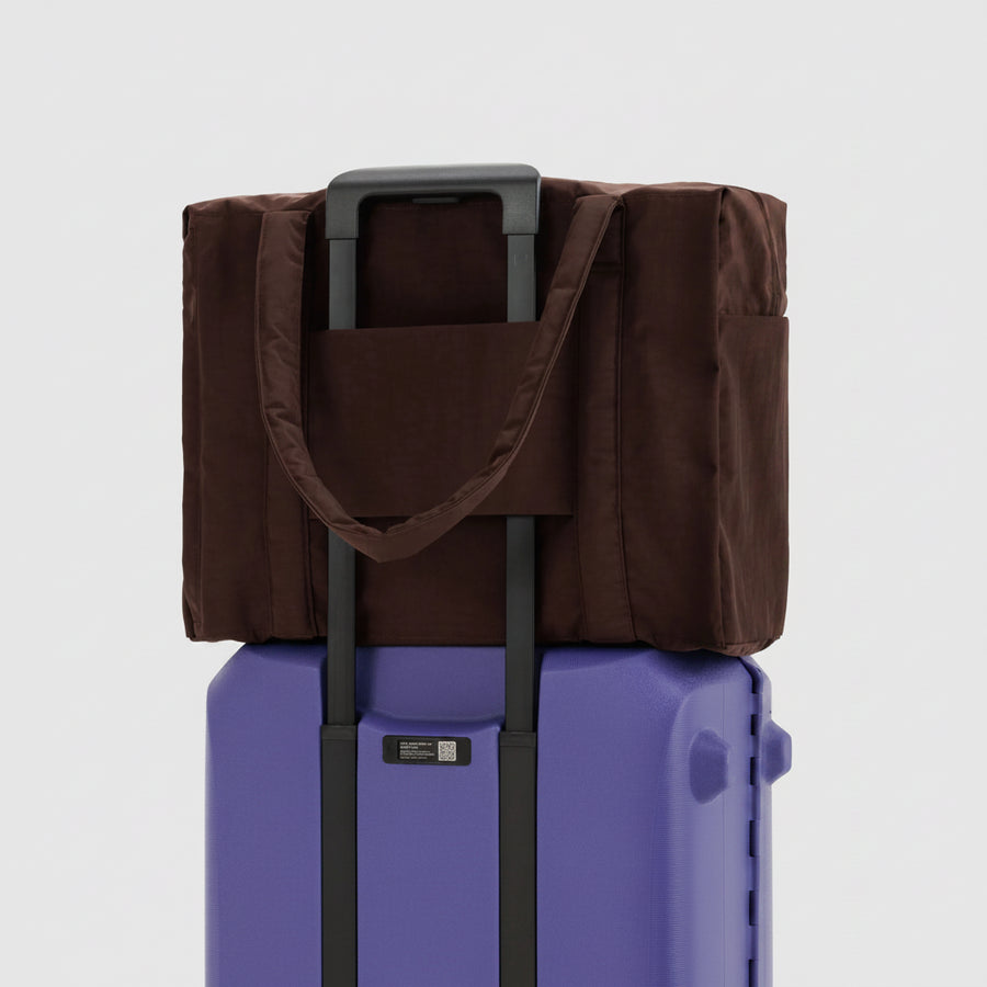 Brown bag with a handle on top of a purple suitcase against a white background