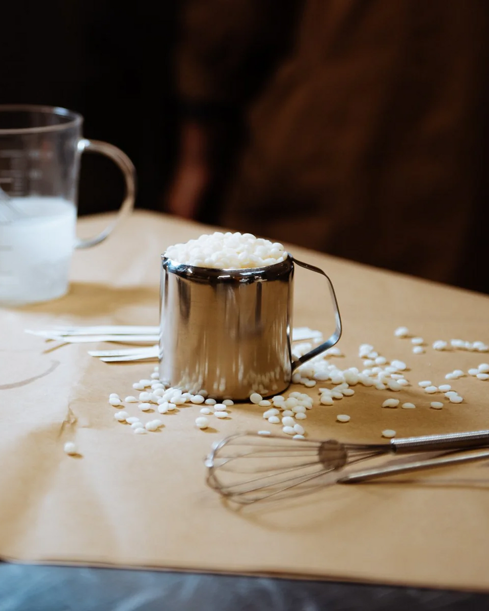 Candle making workshop table with a steel pouring jug and scattered wax flakes