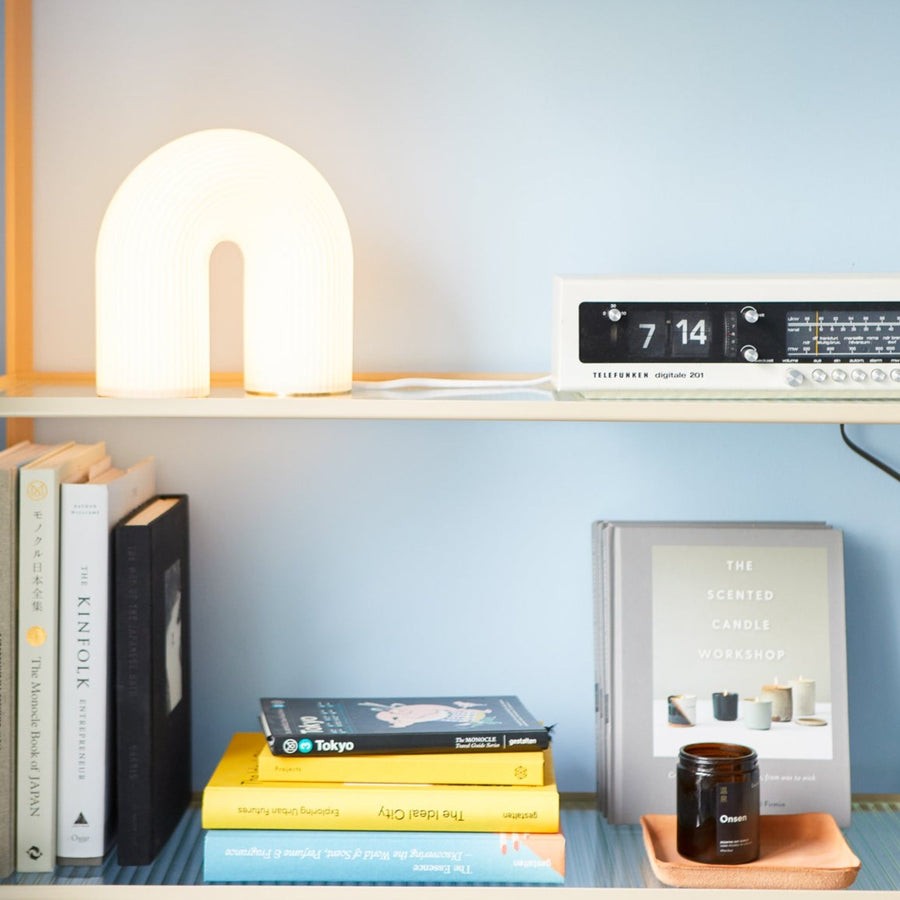 Vuelta Table Lamp by ferm LIVING, lit on a bookshelf