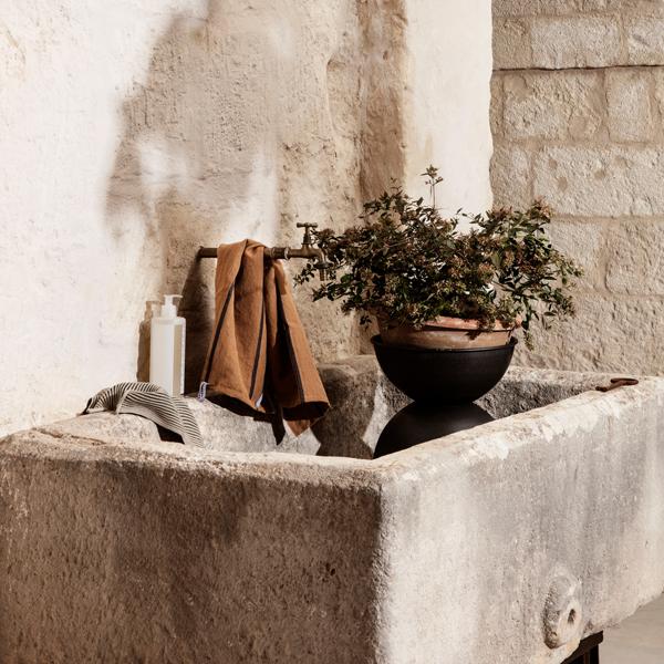 Hourglass Pots, Various Sizes, Black / Dark Grey by ferm LIVING, holding a plant on a stone wall