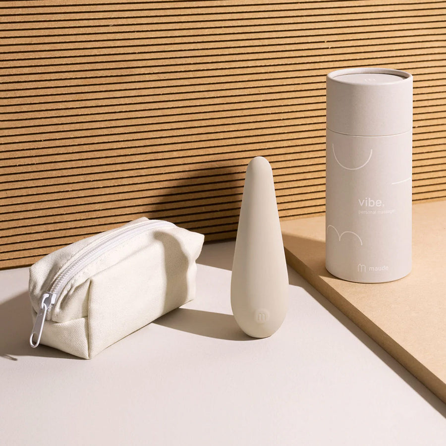 Vibe Personal Massager, Grey by Maude, with its pouch on a beige backdrop